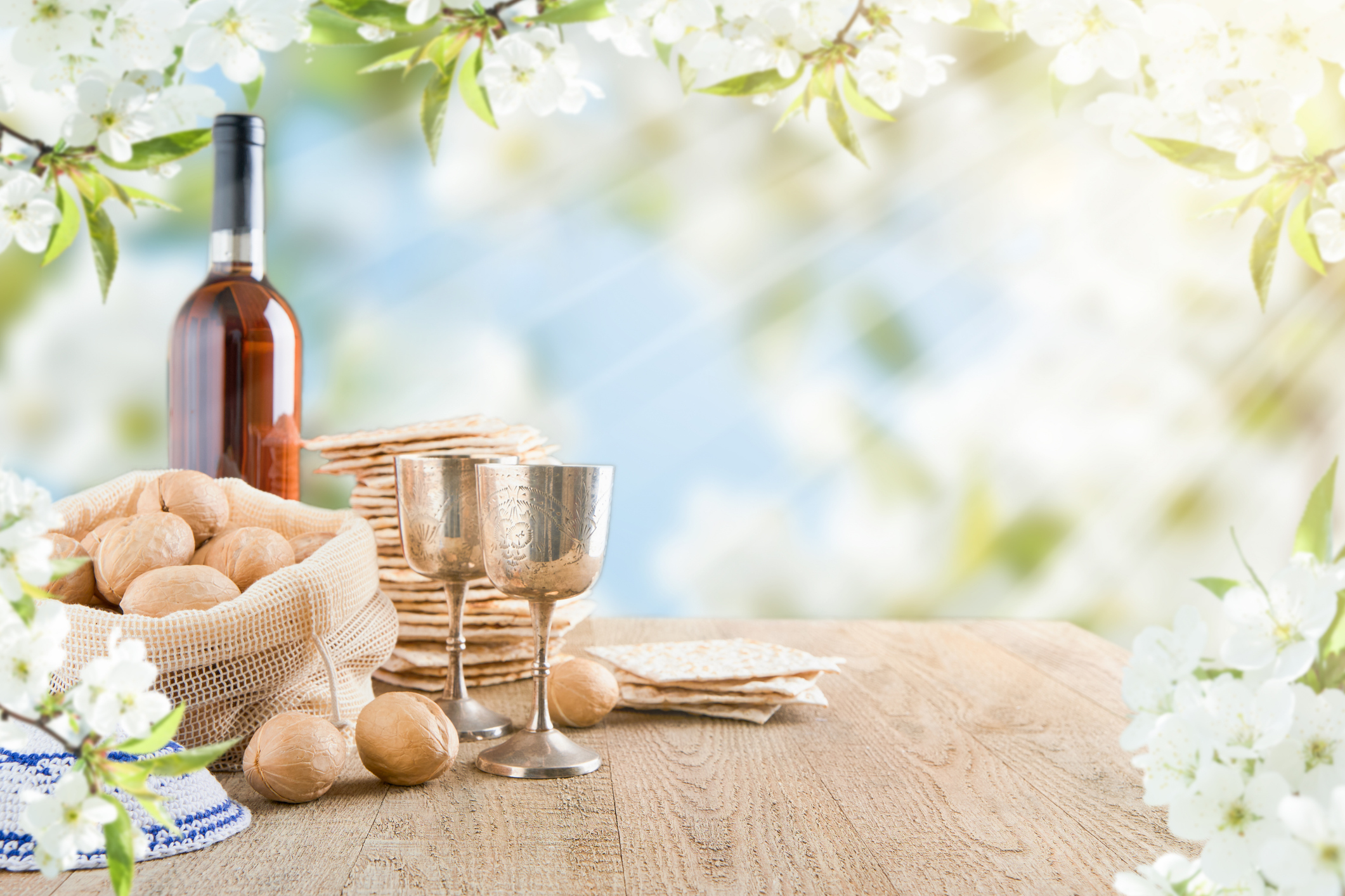 Passover celebration concept. Matzah, red kosher and walnut on wooden vintage table table in front of spring blossom tree garden and flowers landscape with sun rays.